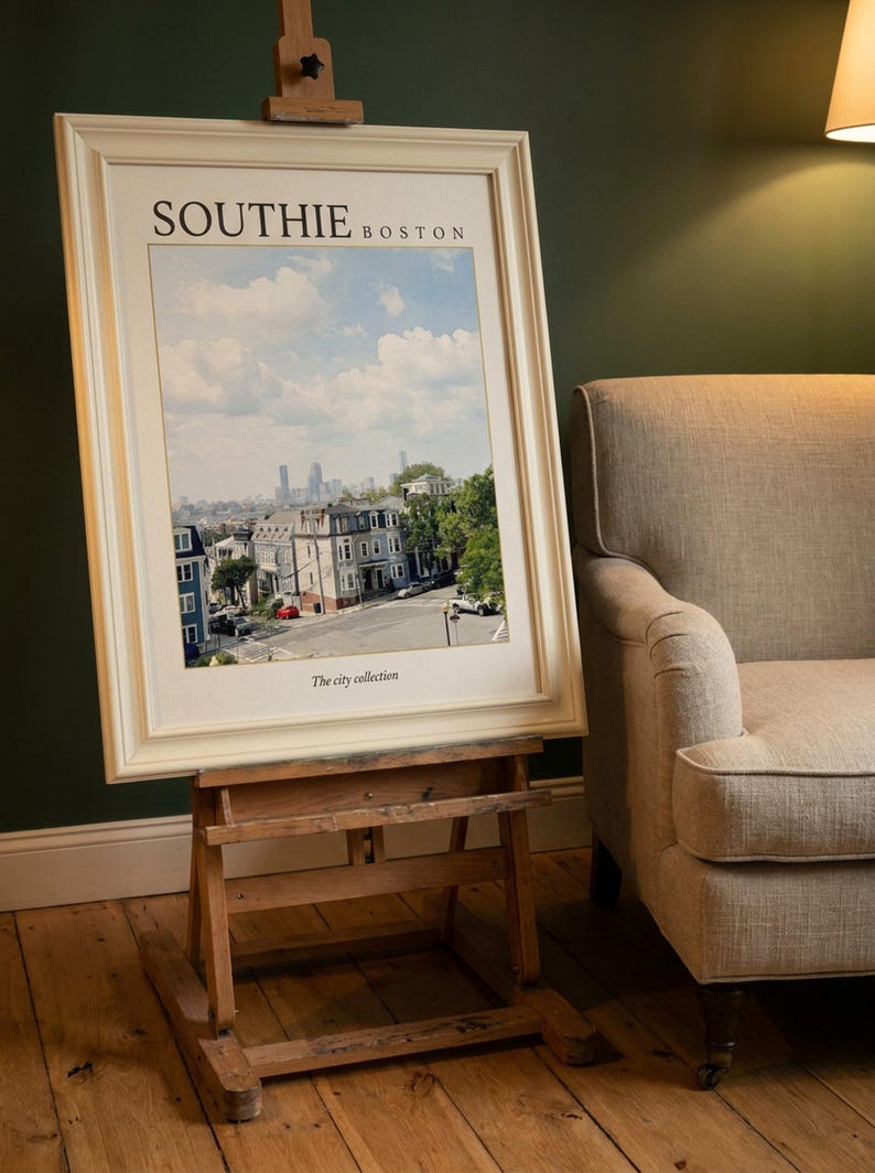 May include: A framed print titled SOUTHIE BOSTON featuring a cityscape view of residential buildings and a distant skyline under a blue sky with clouds. The text The city collection is printed at the bottom of the white matting within the frame.