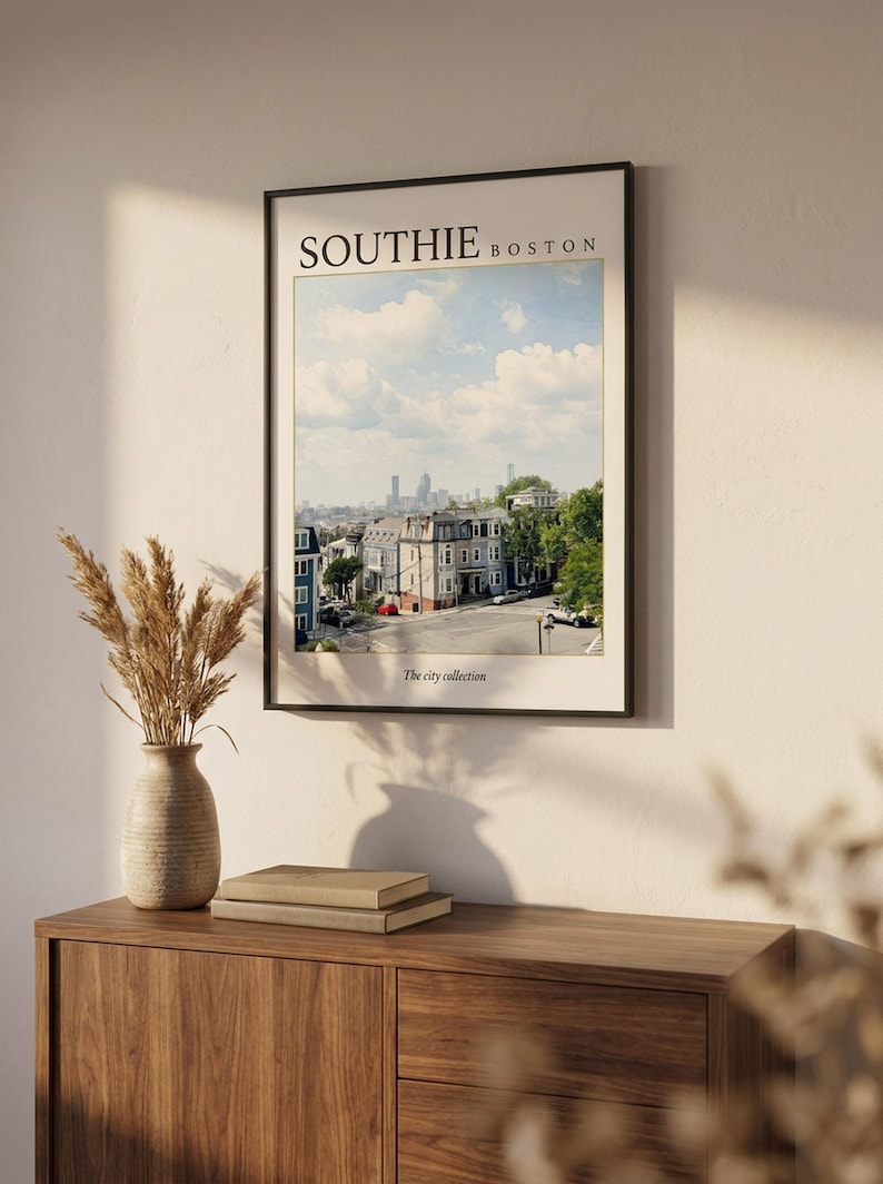 May include: A framed wall art print featuring a photograph of a South Boston neighborhood street scene under a blue sky with clouds. The text SOUTHIE BOSTON is printed at the top, and The city collection is printed at the bottom of the print.