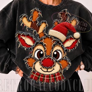 May include: A charcoal grey crewneck sweatshirt featuring a large, frayed-edge appliqué of a reindeer face. The reindeer wears a red Santa hat and a red and green plaid scarf. The design includes brown, red, and cream fabric patches with visible stitching.