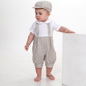 Puede incluir: Una gorra plana de color beige, una camisa blanca de manga corta con cuello redondo y un pantal&oacute;n corto con tirantes de color beige con botones en la parte delantera. El conjunto presenta una tela texturizada y un corte cl&aacute;sico.