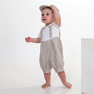 Puede incluir: Un conjunto de peto de lino beige que incluye una camisa blanca de manga corta con cuello redondo y una gorra beige a juego. El peto tiene tirantes anchos sujetos con botones blancos y un dobladillo fruncido con botones a presi&oacute;n.