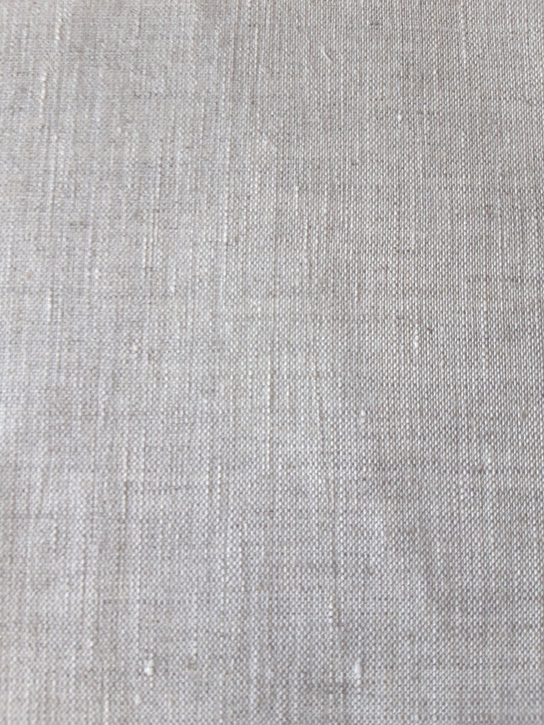Puede incluir: Una vista de cerca de una tela de color beige claro con una textura tejida visible. El material presenta un patr&oacute;n de cuadr&iacute;cula consistente creado por hilos entrelazados, mostrando variaciones naturales en el grosor y color de las fibras.