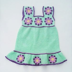 May include: A light green crochet dress with purple and yellow flower accents. The dress has a sleeveless design and a ruffled hem.