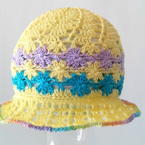 May include: A yellow crocheted sun hat with a brim. The hat has a band of purple and blue crocheted flowers around the crown.