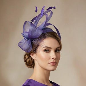May include: A vibrant purple fascinator hat featuring structured sinamay loops, delicate feathers, and a fine netting veil. The headpiece is paired with a matching purple long-sleeved dress that has a simple round neckline and subtle pleating.