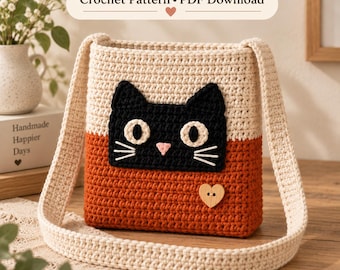 May include: A crochet bag featuring a two-tone design with a cream upper section and a rust-colored lower section. A black cat face applique with white eyes and whiskers is centered on the front, accented by a small wooden heart-shaped button.
