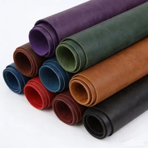 May include: A collection of rolled leather sheets in various colors including purple, dark green, brown, blue, red, and black. Each roll displays a smooth, matte surface texture with visible edges showing the natural thickness of the material.
