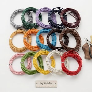 Könnte beinhalten: Eine Sammlung von fünfzehn aufgerollten Lederschnüren in verschiedenen Farben, darunter Grau, Grün, Lila, Marineblau, Kastanienbraun, Gelb, Orange, Blau, Braun, Rosa, Oliv, Weiß und Rot. Eine Metallzange und ein Etikett mit Tiny Tails Leather 2mm Assortment.