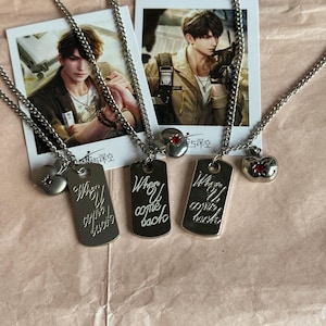 May include: Three silver-toned metal necklaces featuring rectangular dog tags engraved with the text When U come back. Each necklace includes a small apple-shaped charm with a single embedded red stone. The chains are linked to the pendants.