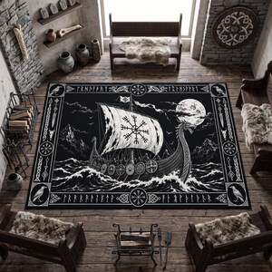 Op de afbeelding: Een rechthoekig vloerkleed met een zwart-witte illustratie van een Vikingschip dat onder een volle maan op woelige golven vaart. Het ontwerp bevat een zeil met een Vegvisir-symbool, een boeg met drakenkop en een rand met runeninscripties.