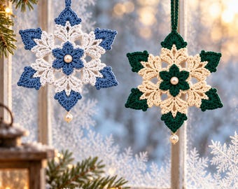 May include: Two six-pointed star-shaped crochet ornaments hanging from a pine branch. One ornament is blue and white, the other is dark green and cream. Each features a central white pearl bead and a single pearl bead dangling at the bottom.