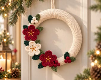 May include: A circular wreath wrapped in cream-coloured cord, decorated with crocheted dark red and cream flowers, dark green leaves, and small white and red berries. The wreath features a hanging loop at the top and is suspended on a door hook.