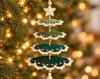 May include: A hanging Christmas tree ornament crafted from crocheted layers in shades of green, featuring a cream-coloured star at the top, small gold-toned beads between each tier, and a cream-coloured tassel hanging from the bottom.