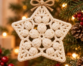 May include: A cream-coloured star-shaped crochet ornament featuring a central flower motif made of puff stitches. The star is suspended by a natural jute twine loop tied in a small bow at the top, showcasing intricate yarn work and texture.