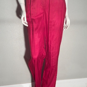 Può includere: Un paio di pantaloni magenta vivaci con taglio a gamba dritta, design a vita alta con sottili pieghe frontali e una cucitura verticale visibile lungo il centro di ogni gamba, abbinati a un top in maglia bianca testurizzata.
