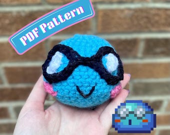 Puede incluir: Un juguete de peluche tejido a ganchillo de color azul brillante, de forma redonda, con gafas blancas de montura negra, una pequeña boca negra bordada y mejillas rosas bordadas. La imagen incluye el texto "PDF Pattern" y "AbiesCustomDesigns" junto a un icono de slime azul pixelado.