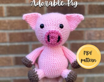 Puede incluir: Un cerdo de ganchillo rosa con ojos negros, un hocico rosa más oscuro y pezuñas marrones. El texto Adorable Pig está en la parte superior, y un círculo amarillo con el texto PDF pattern a la derecha. El texto PigeonPatternCrochet está abajo.