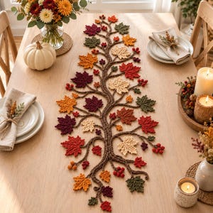 May include: A crochet table runner featuring a central brown branch design adorned with various autumn-colored leaves in shades of red, orange, yellow, and green, accented with small clusters of red berries, laid flat on a wooden table.