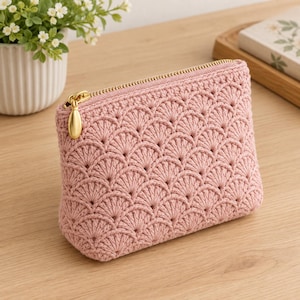 Può includere: Una pochette all'uncinetto color rosa polvere caratterizzata da un motivo a ventaglio ripetuto. L'accessorio rettangolare è chiuso da una cerniera in metallo dorato con una linguetta liscia a forma di goccia sul bordo superiore.