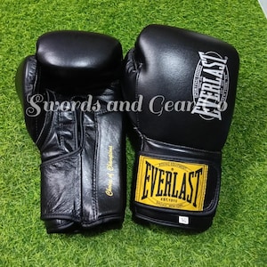 Può includere: Un paio di guantoni da boxe neri Everlast con marchio bianco e una toppa gialla sul cinturino da polso. I guantoni presentano la scritta Everlast, Choice of Champions e una piccola etichetta bianca che indica 16 oz. Finitura liscia.