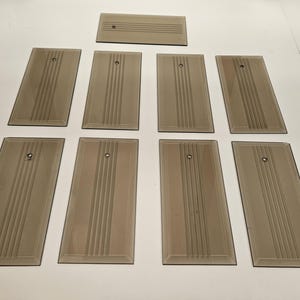May include: A set of nine rectangular, smoke-tinted glass wall plates. Each plate features a central vertical column of three etched parallel lines and a single small, centered metal mounting hole near the top edge of the glass surface.