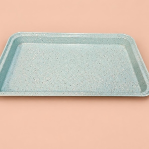 May include: A rectangular baking tray with a light blue speckled finish. The tray features a flat base and slightly raised, angled edges, showcasing a consistent mottled texture across the entire interior and exterior surface.