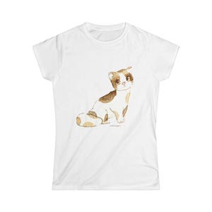 May include: A white short-sleeved t-shirt featuring a watercolor-style illustration of a small cat with brown and white patches. The cat is depicted in a sitting position, facing forward with large dark eyes and a small pink nose on the chest area.