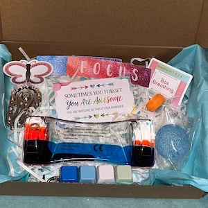 May include: A cardboard gift box filled with white paper shred, containing a blue liquid motion bubbler, a card reading Sometimes You Forget You Are Awesome, a butterfly-shaped sticker, a Box Breathing instruction card, and four small colored cubes.