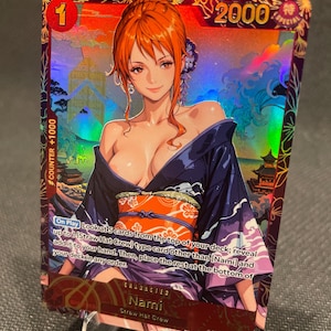 May include: A holographic One Piece trading card featuring Nami in a dark blue kimono with an orange obi. The card displays the text Nami, Straw Hat Crew, and game instructions. It has a red number 1, a 2000 power value, and a counter +1000 icon.