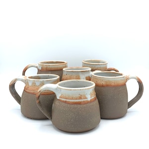 May include: Six brown and white ceramic mugs with a speckled glaze. The mugs have a rounded shape and a wide handle.