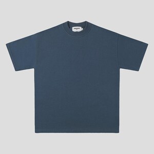 Peut inclure: Un t-shirt bleu ardoise uni à manches courtes avec un col rond épais et côtelé. Le vêtement présente une coupe carrée et ample avec des manches à ourlet droit et un bas droit. Une étiquette de marque blanche est visible dans le col.