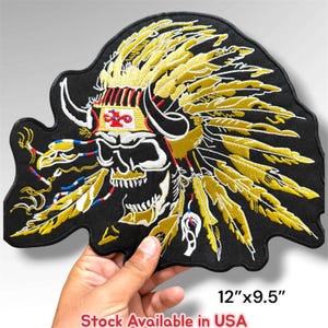 May include: An embroidered patch featuring a skull wearing a large yellow and gold feathered headdress with black horns. The design includes a white headband with a red cross symbol and dangling feathers with blue and red accents. Measures 12"x9.5".
