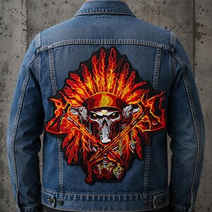 May include: A blue denim jacket featuring a large embroidered back patch. The patch displays a skull wearing a helmet, surrounded by a vibrant red and orange feathered headdress and crossed axes, all set against a black background.
