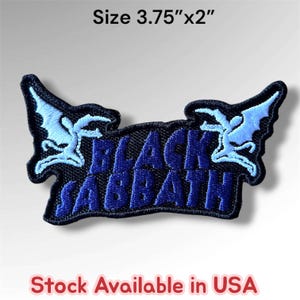 May include: An embroidered patch featuring the text Black Sabbath in dark blue thread on a black background, flanked by two light blue winged figures. The patch measures 3.75 inches by 2 inches and is designed for application to fabric surfaces.