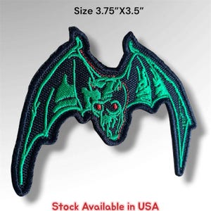 May include: An embroidered patch featuring a stylized bat design with black fabric, vibrant green wing outlines, and red eyes. The patch measures 3.75 inches by 3.5 inches and includes the text Size 3.75"X3.5" and Stock Available in USA.