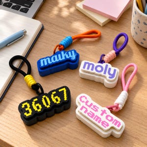 Può includere: Quattro portachiavi rettangolari con testo pixelato e anelli colorati. I portachiavi presentano le scritte maiky in blu, moly in viola, 36067 in giallo e Custom name in rosa. Ogni portachiavi ha un cordino con un dettaglio avvolto.