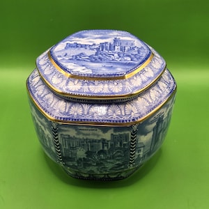 May include: A hexagonal ceramic jar with a lid, featuring blue and white transferware patterns of Durham Castle. The design includes intricate floral borders and gold-toned trim along the edges of the lid and the upper rim of the jar body.