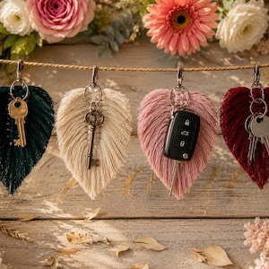 Peut inclure: Quatre porte-clés en macramé en forme de feuille, de couleurs vert foncé, crème, vieux rose et rouge foncé, suspendus à une cordelette. Ils sont dotés de mousquetons et d'anneaux métalliques retenant diverses clés et un boîtier de clé de voiture.