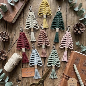Könnte beinhalten: Eine Sammlung von acht Makramee-Baum-Schlüsselanhängern in verschiedenen Farben wie Gelb, Dunkelgrün, Burgunderrot, Altrosa, Hellblau, Salbeigrün und Creme, jeweils mit einem silbernen Karabinerverschluss und einer geknoteten Quaste.