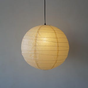 May include: A spherical paper lantern pendant light with a cream-colored shade. The shade features a delicate, thin wire frame structure wrapped in textured paper, suspended from a single thin black cord against a plain gray background.