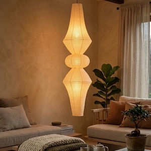 May include: A tall, vertical pendant lamp made of off-white paper with a ribbed texture. The lamp features a stacked, multi-sectioned silhouette with two large, tapered, diamond-shaped forms separated by a smaller, rounded, central bulbous section.