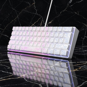 May include: A white mechanical keyboard featuring a topographic map pattern on the keycaps. The keys display standard QWERTY lettering and symbols, with integrated RGB lighting that casts a soft glow beneath the keys and a white cable extending upwards.