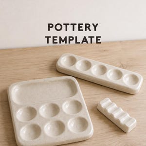 Puede incluir: Un conjunto de tres plantillas de cerámica de color blanco roto con motas. Una bandeja cuadrada presenta seis hendiduras circulares y una sección rectangular. Una bandeja rectangular larga tiene cinco hendiduras. Una herramienta pequeña tiene cuatro ranuras.
