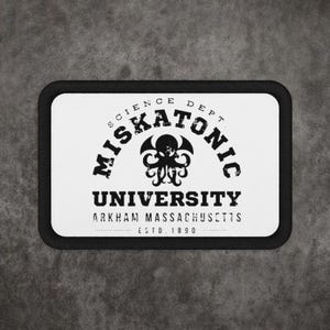 May include: A rectangular patch with a black border and white background. The text reads MISKATONIC UNIVERSITY, SCIENCE DEPT, ARKHAM MASSACHUSETTS, ESTD 1890. A black graphic of a tentacled creature with wings is centered between the text lines.