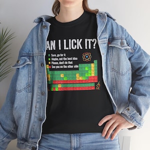 以下が含まれることがあります： 黒いTシャツ。白い文字で「CAN I LICK IT?」と書かれ、その下に周期表のグラフィックがある。色分けされた安全警告があり、緑は「sure, go for it」、青は「maybe, not the best idea」、黄色は「please, don't do that」、赤は「see you on the other side」と記されている。