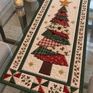 May include: A rectangular quilted table runner featuring a central Christmas tree design composed of layered fabric triangles in red, green, and cream patterns. The tree is topped with a gold star and accented with small red pom-poms.