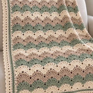 May include: A crocheted blanket featuring a repeating scalloped shell pattern in alternating horizontal stripes of cream, beige, and sage green. The blanket is finished with a decorative border consisting of a thin green line and a cream scalloped edge.