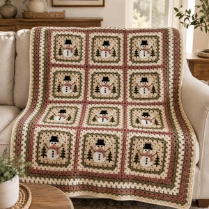 May include: A crochet blanket featuring a repeating pattern of twelve square motifs. Each square displays a white snowman with a black top hat, a pink scarf, and brown stick arms, flanked by two small green pine trees on a cream background.