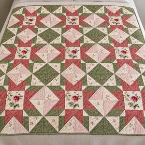 May include: A patchwork quilt featuring a repeating geometric star pattern. The design incorporates sage green, dusty rose, and cream fabric squares. Some cream squares are printed with small red rose floral motifs and green leaves.