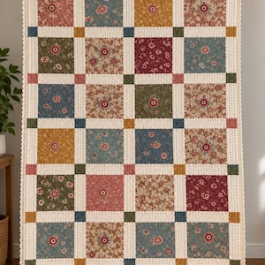 May include: A rectangular quilt featuring a grid of square fabric patches with various floral patterns in shades of blue, pink, mustard yellow, and deep red. The squares are separated by cream-coloured sashing with small coloured corner squares.